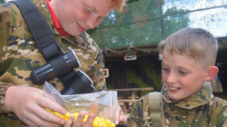 junior paintballer helping another load paintballs